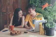 Young Couple Having Coffee And Chocolate Braids Using Laptop At Home