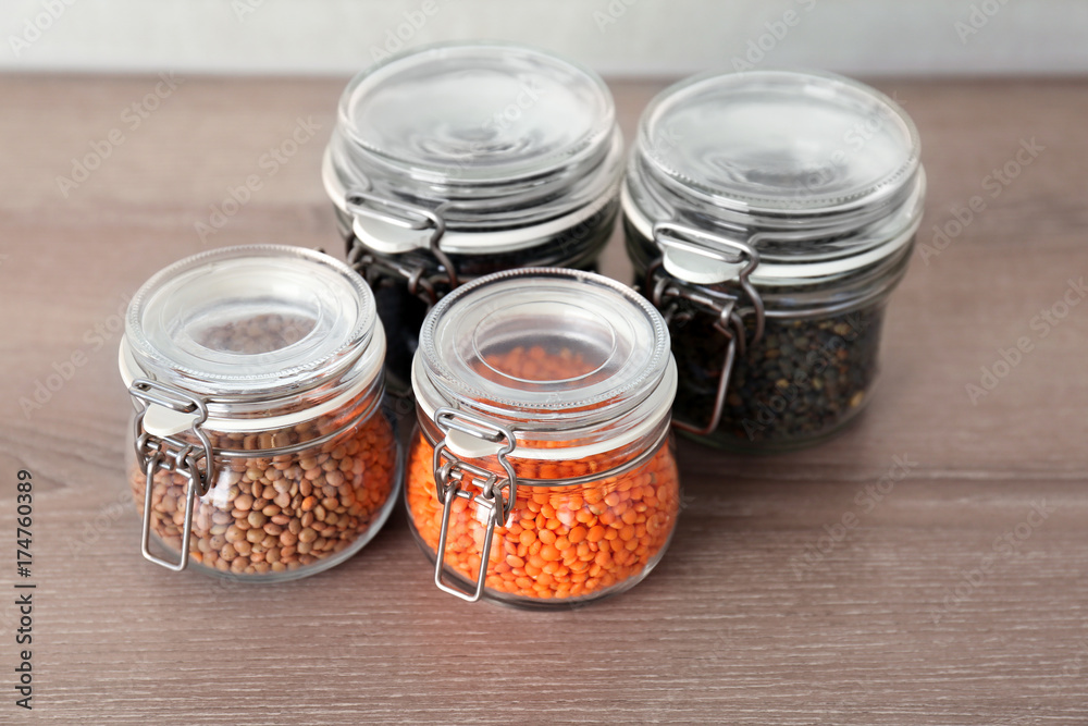 Different types of lentils in glass jars on wooden table