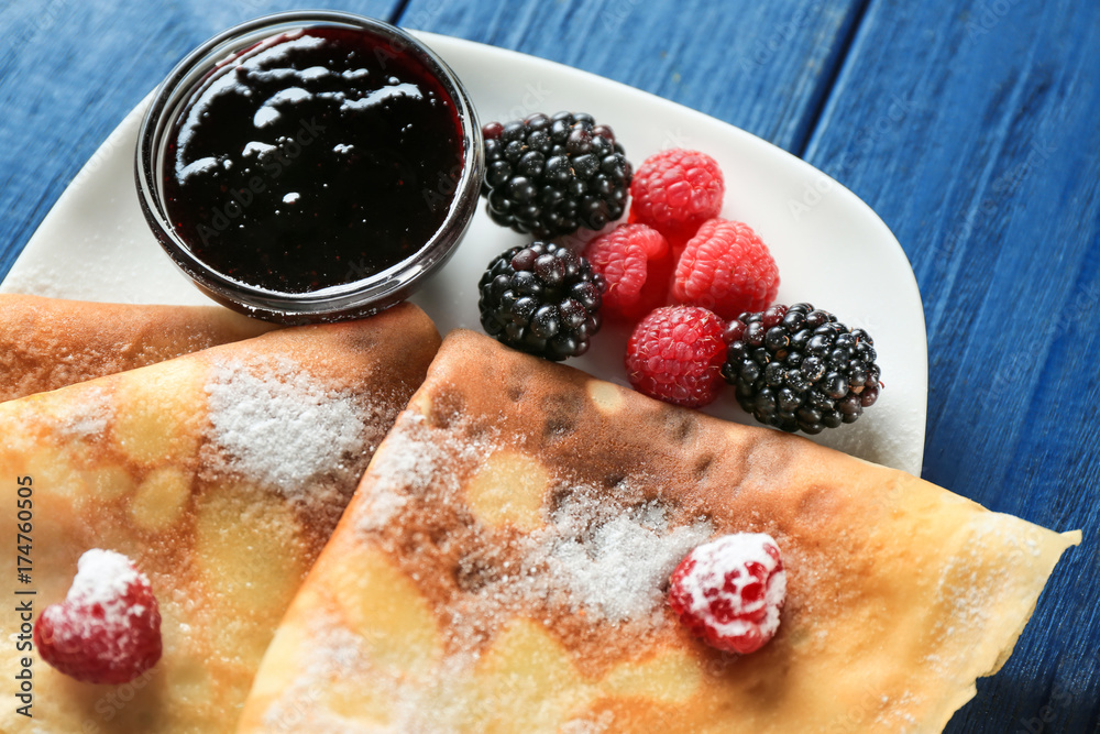 Plate of delicious thin pancakes with berries and jam on table, closeup