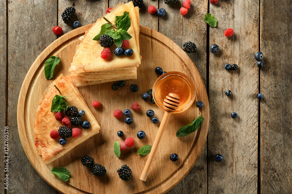 Board with tasty thin pancakes and berries on table
