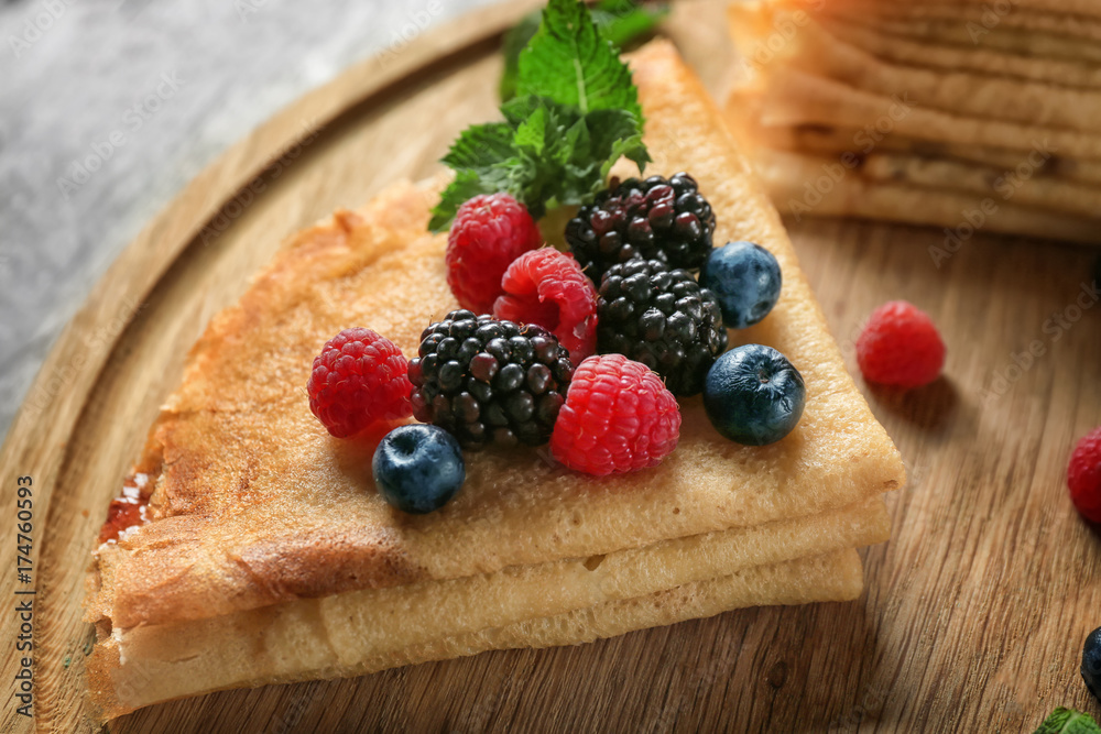 Tasty thin pancakes with berries on wooden board, closeup
