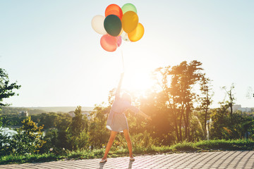 Cute girl holding colorful balloons in the city park, staying in