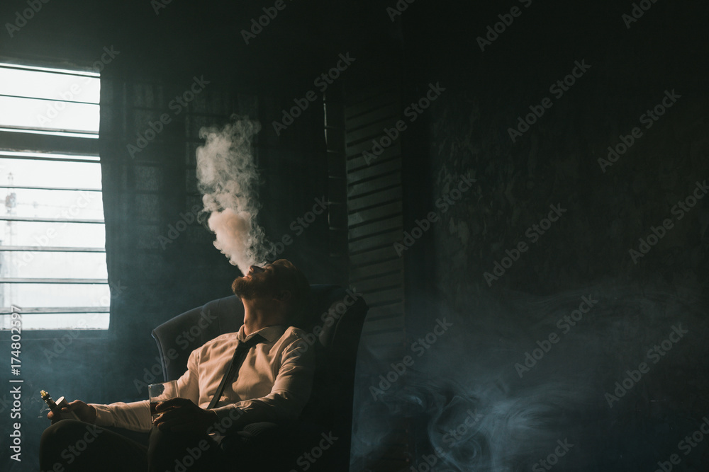 Businessman relaxing with vape and alcohol. Dark room with white  atmospheric smoke background, rich people entertainment, private club for  luxury life with free space Stock Photo