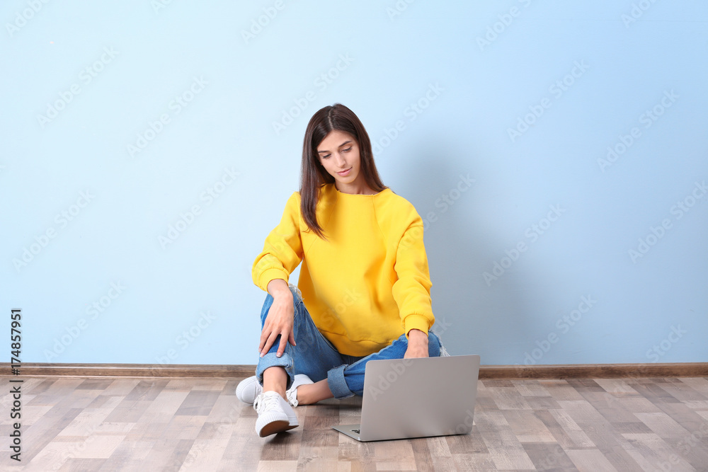 Young woman with laptop near color wall