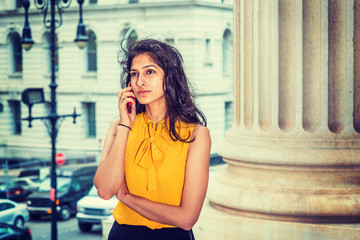 East Indian American Business Woman working in New York. Wearing sleeveless orange shirt, a college student calling on cell phone on street, many cars on background. Instagram filtered effect..