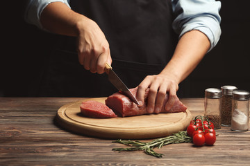 Wall Mural - Chef cutting fresh raw meat on wooden board