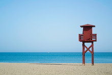 Red Wooden Lifeguard Tower On The Abandoned Beach At Benalmadena, Malaga Province, Spain. Beautiful View Of The Sea And Sandy Beach On Sunny Summer Day With Copy Space.