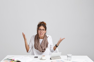 Wall Mural - Too much workload and file error. Stylish female employee having bad day at work, sitting at desk with electronic gadgets, mug and glass, feeling annoyed as she doesn't have time to drink her espresso