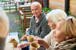 © Seventyfour - Portrait of handsome senior man with deep blue eyes listening to his friend with interest while having good time together at outdoor cafe, pretty women sitting next to him and enjoying fragrant coffee