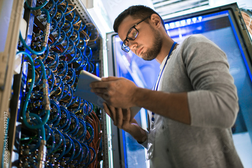 Fotografía Low angle portrait of young man using digital tablet standing by server cabinet