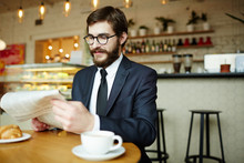 Bearded Man In Elegant Suit And Eyeglasses Sitting In Cafe And Reading Newspaper