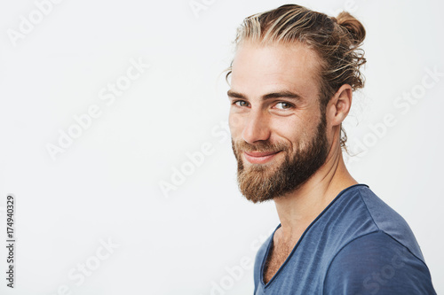 Fotografie, Obraz Close up portrait of handsome manly guy with beard posing in three quarters, looking in camera and happily smiling