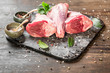 Raw lamb shanks with salt and pepper on stone tray on rustic wooden table. selective focus