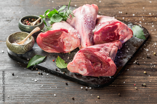 Cuadros en Lienzo Raw lamb shanks with salt and pepper on stone tray on rustic wooden table