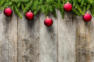 Christmas fir tree with decorations on wooden background. Red ornaments hanging on branches on old wooden boards