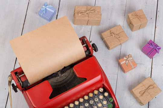 Holidays concept - red typewriter with blank craft paper, gift boxes on white wooden background