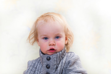 Wall Mural - baby (2 years old) blond boy with long hair in a warm gray sweater