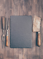 Wall Mural - Slate coaster with vintage meat cleaver and fork on wooden background with copy space