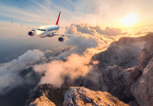 Airplane Is Flying Over Clouds At Sunset. Landscape With White Passenger Airplane, Mountains, Sea And Orange Sky With Sun In Summer. Passenger Aircraft Is Landing. Business Travel. Commercial Plane