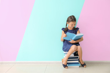 Wall Mural - Cute little girl reading books near color wall