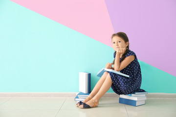 Canvas Print - Cute little girl reading books near color wall