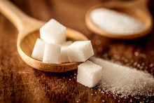 Close Up White Sugar Cubes And Cane In Wooden Spoon On The Table