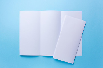 Leaflet blank tri-fold white paper brochure mockup on blue background. top view
