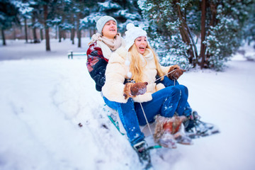  A young couple is riding a sled in the snow in a park in the winter.