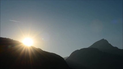 Wall Mural - Track from a flying airplane like a comet flying through the sky. Sun with bright rays against a clear blue sky. Sunset at the top of the mountains.