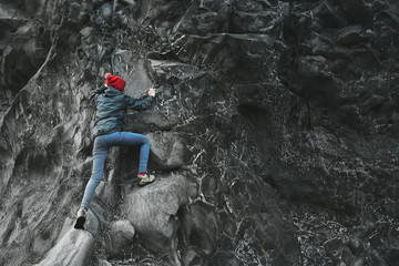 Wall Mural - woman rock climber. rock climber climbs on a black rocky wall on the ocean bank in Iceland, Kirkjufjara beach. woman makes hard move without rope.