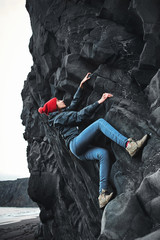 Wall Mural - woman rock climber. rock climber climbs on a black rocky wall on the ocean bank in Iceland, Kirkjufjara beach. woman makes hard move without rope.