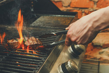Man Cooking Meat Steaks On Professional Grill Outdoors