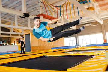 Happy emotional man jumping and flying in trampoline sport center indoors