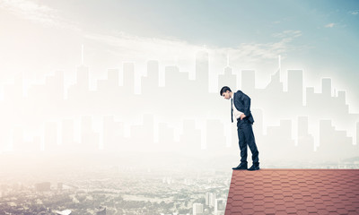 Businessman looking down from roof and modern cityscape at backg