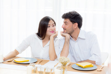 Cheerful asian young man and woman having sitting lunch and talking  together at kitchen