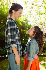 Wall Mural - Side view of smiling mother and daughter standing in backyard