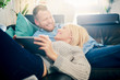 © chika_milan - Couple using tablet while laying on sofa in living room