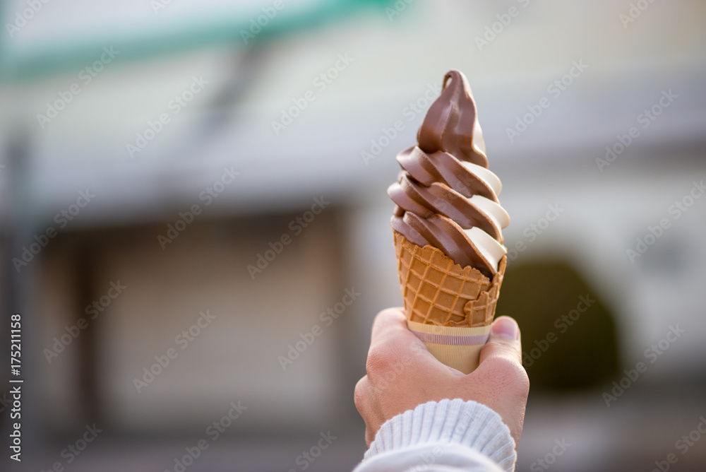 Close-up detail of a chocolate vanilla twist soft serve in a crispy, homemade waffle cone, with blurred background and sweater hands. Nobeoka, Japan. Travel and food concept. - obrazy, fototapety, plakaty 