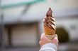 Close-up detail of a chocolate vanilla twist soft serve in a crispy, homemade waffle cone, with blurred background and sweater hands. Nobeoka, Japan. Travel and food concept.