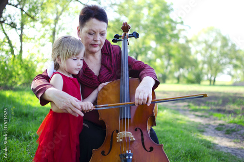 Zdjęcie XXL Babcia i wnuczka gra na zewnątrz na wiolonczeli. Dorosła kobieta naucza dziewczynę bawić się violocello