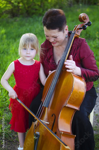 Zdjęcie XXL Babcia i wnuczka gra na zewnątrz na wiolonczeli. Dorosła kobieta naucza dziewczynę bawić się violocello
