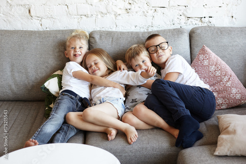Fotografie, Obraz Cozy sweet shot of four siblings cuddling at home: three brothers hugging tight their little sister, expressing love, tenderness and affection towards each other