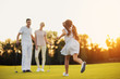 © VadimGuzhva - The girl runs across the golf course towards the man and woman who stand in front of her and golf clubs