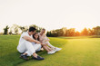 © VadimGuzhva - Happy family resting on a golf course sitting on the grass on a sunset background