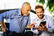 © VadimGuzhva - Old man in a wheelchair and a man looking at something in a tablet walking in the park. Old man shows something to a man