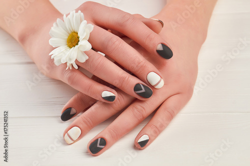 Zdjęcie XXL Zadbane dłonie i biała chryzantema. Kobiet ręki z matte manicure i małym kwiatem na białym drewnianym tle. Leczenie paznokci i spa.