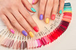 Summer manicure and nail color samples. Young woman hands with multicolored manicure and collection of color nail polish samples. Nail beauty salon.
