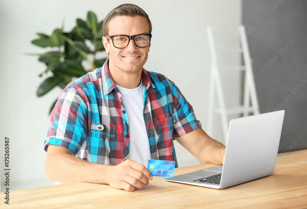 Young man holding credit card while using laptop at home