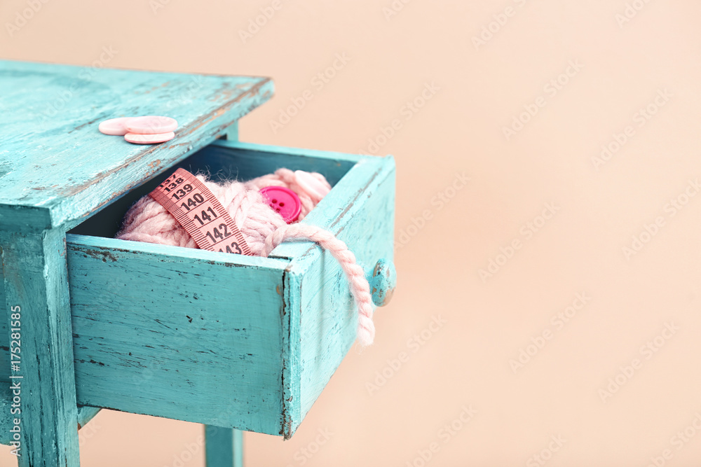 Drawer with pink crafting accessories on apricot background