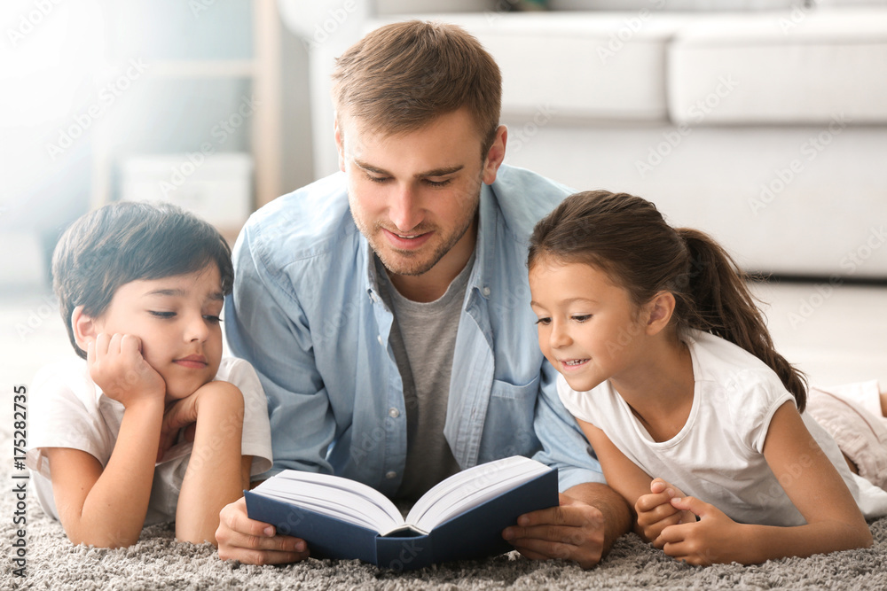 Young man and his little children reading book at home